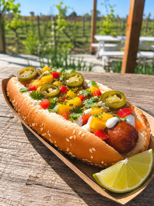 The Mango Salsa Dog at Traynor Family Vineyard - an all-beef hot dog on a sesame bun topped with house-made mango salsa, diced red pepper, pickled jalapeno, cilantro, and crema