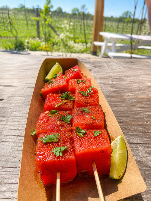 Watermelon Tajin at Traynor Family Vineyard - watermelon skewers dusted with Tajin chili salt and topped with torn mint and lime, served in a kraft tray with the Hillier vineyard behind