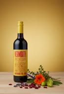 Bottle of vermouth with a yellow label on a wooden surface with flowers and herbs.