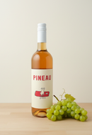 Bottle of Pineau with a label featuring a cow illustration on a wooden surface with grapes.