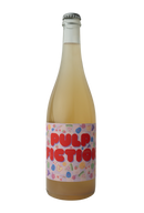 "A bottle of Traynor Family Vineyard's Pulp Fiction wine with a pale yellow hue. The label features bold red text 'PULP FICTION' on a playful pastel background adorned with colorful illustrations of fruits, including watermelon slices, cherries, lemons, and grapes."