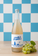 Bottle of 'Chill Thrill' beverage with a label featuring a blue and white design, placed on a wooden surface with a checkered blue and white wall in the background.