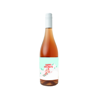 "A bottle of rosé wine with a festive 'Happy Holidays' label. The label features a red and white reindeer skiing down a snowy hill surrounded by green pine trees, evoking a cheerful winter holiday scene."