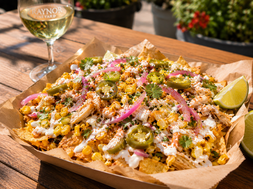 Street Corn Nachos at Traynor Family Vineyard — corn-style nachos with crema, pulled chicken, chili, cilantro, pickled red onion, jalapeños, and lime, with a glass of Traynor wine.