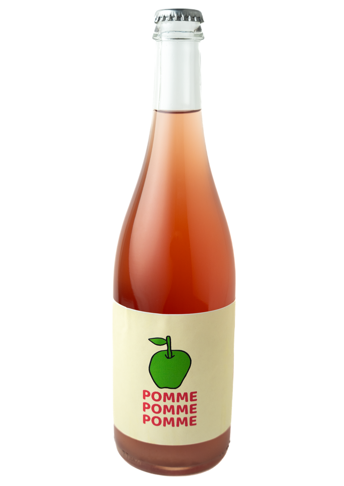 A bottle shot of Pomme Pomme Pomme. the bottle is clear with a silver crown cap, and a rosy hazy wine.  The label is a cream band with a drawing of a green apple and the words Pomme Pomme Pomme below the apple descending to the bottom of the label