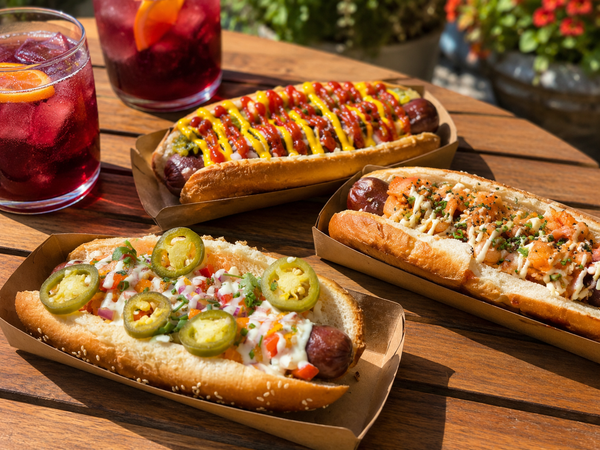 Three Traynor gourmet hot dogs - Classic, Mango Salsa, and Kimchi - with red wine coolers on the patio table at Traynor Family Vineyard, Hillier, Prince Edward County